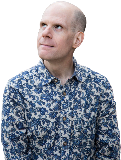 Luke Perone in a patterned shirt with blue and beige floral designs is looking upwards with a thoughtful expression, as if considering a social therapeutic technique. The background is blurred, focusing attention on the man.
